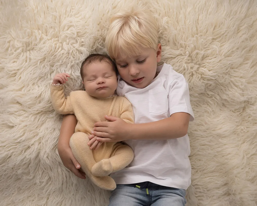 Newborn girl in yellow romper being cuddled by big brother in Sharon Lewis Photography studio Somerset