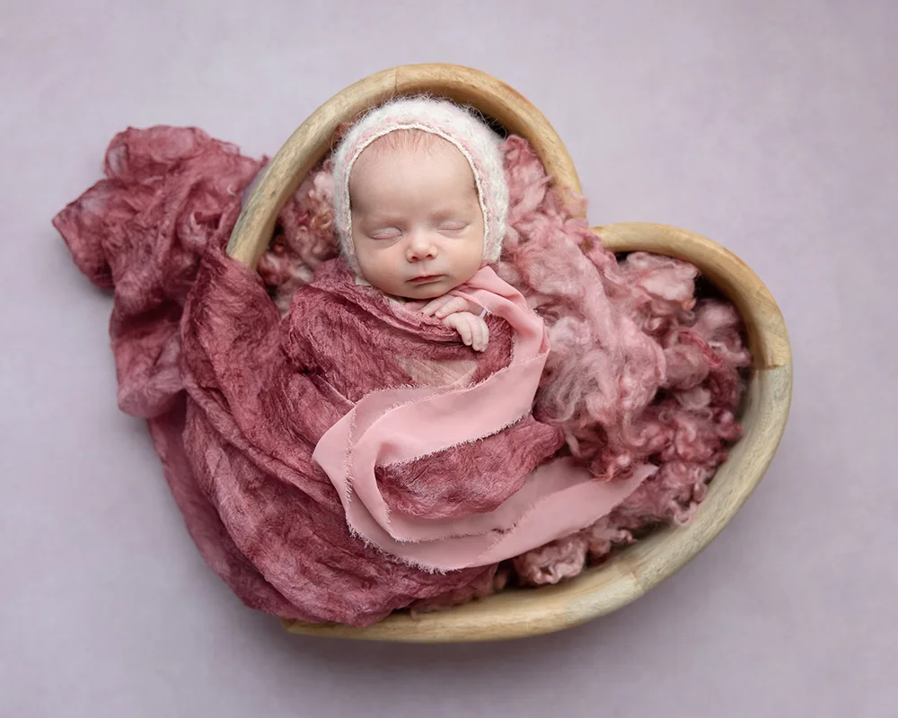 newborn girl in pink heart with pink bonnet