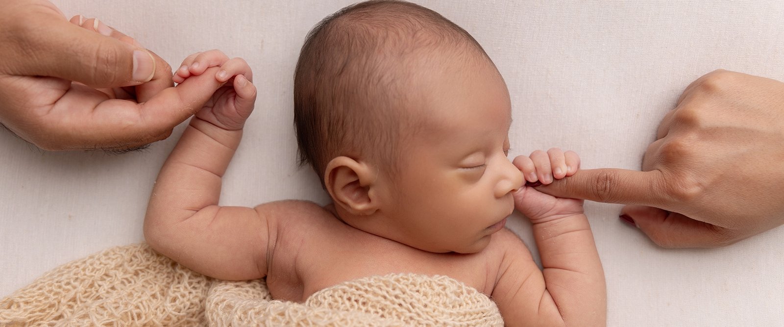 Newborn baby holding parents fingers